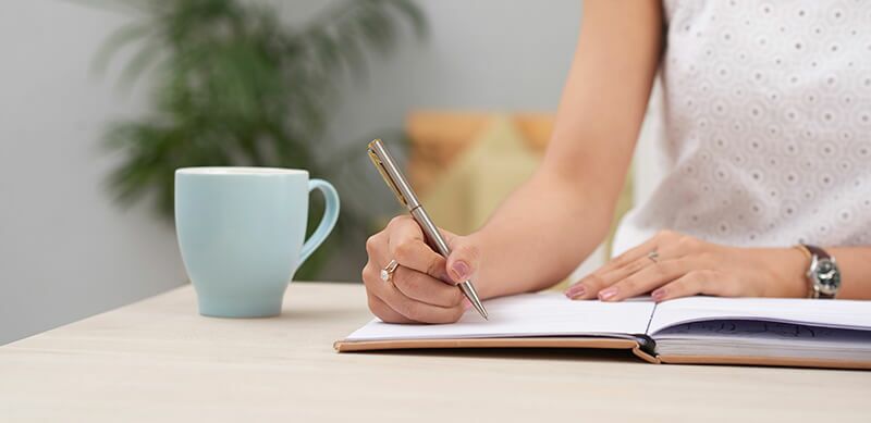 Planejamento anual de acordo com a BNCC: fotografia de uma mulher escrevendo em um caderno.