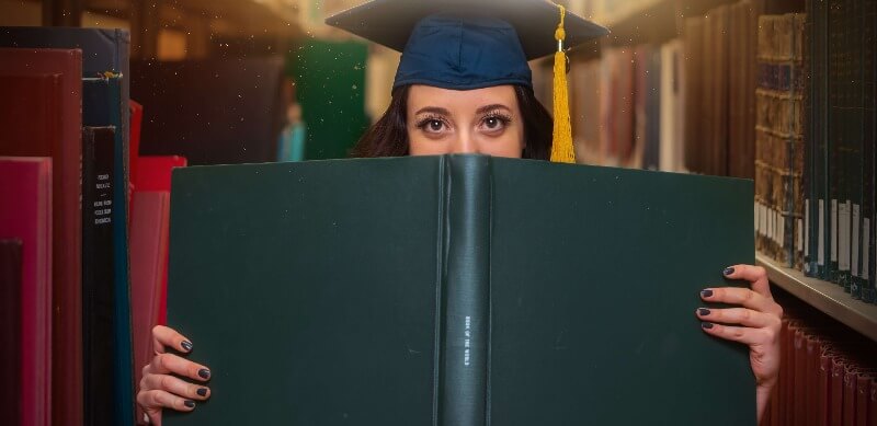 Orientação profissional no ensino médio: fotografia de uma menina usando capelo e segurando um livro.