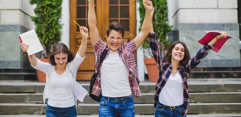 Desempenho escolar: fotografia de três estudantes comemorando.