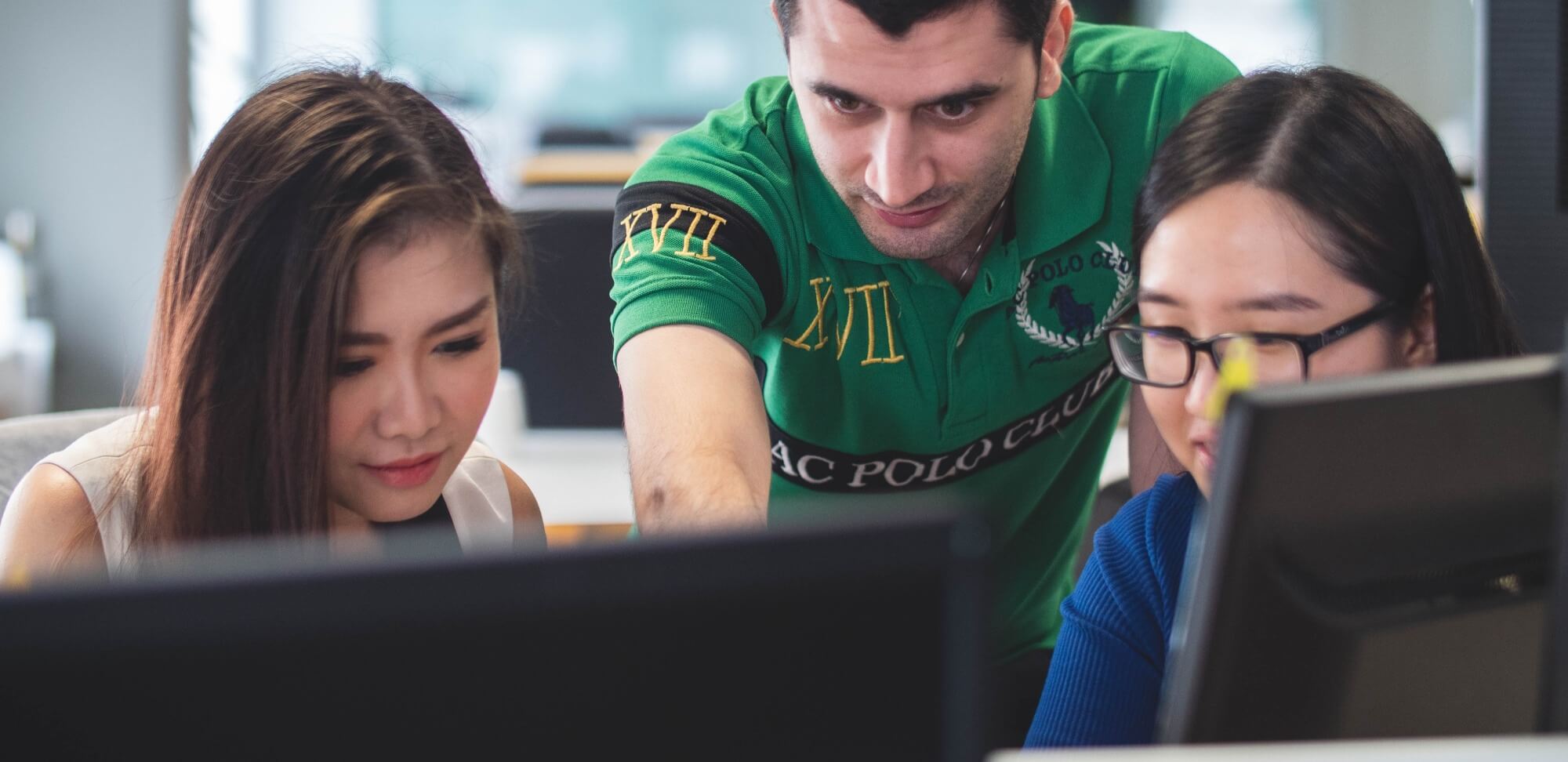 Ensino híbrido: fotografia de duas estudantes usando o computador e um professor mostrando algo.