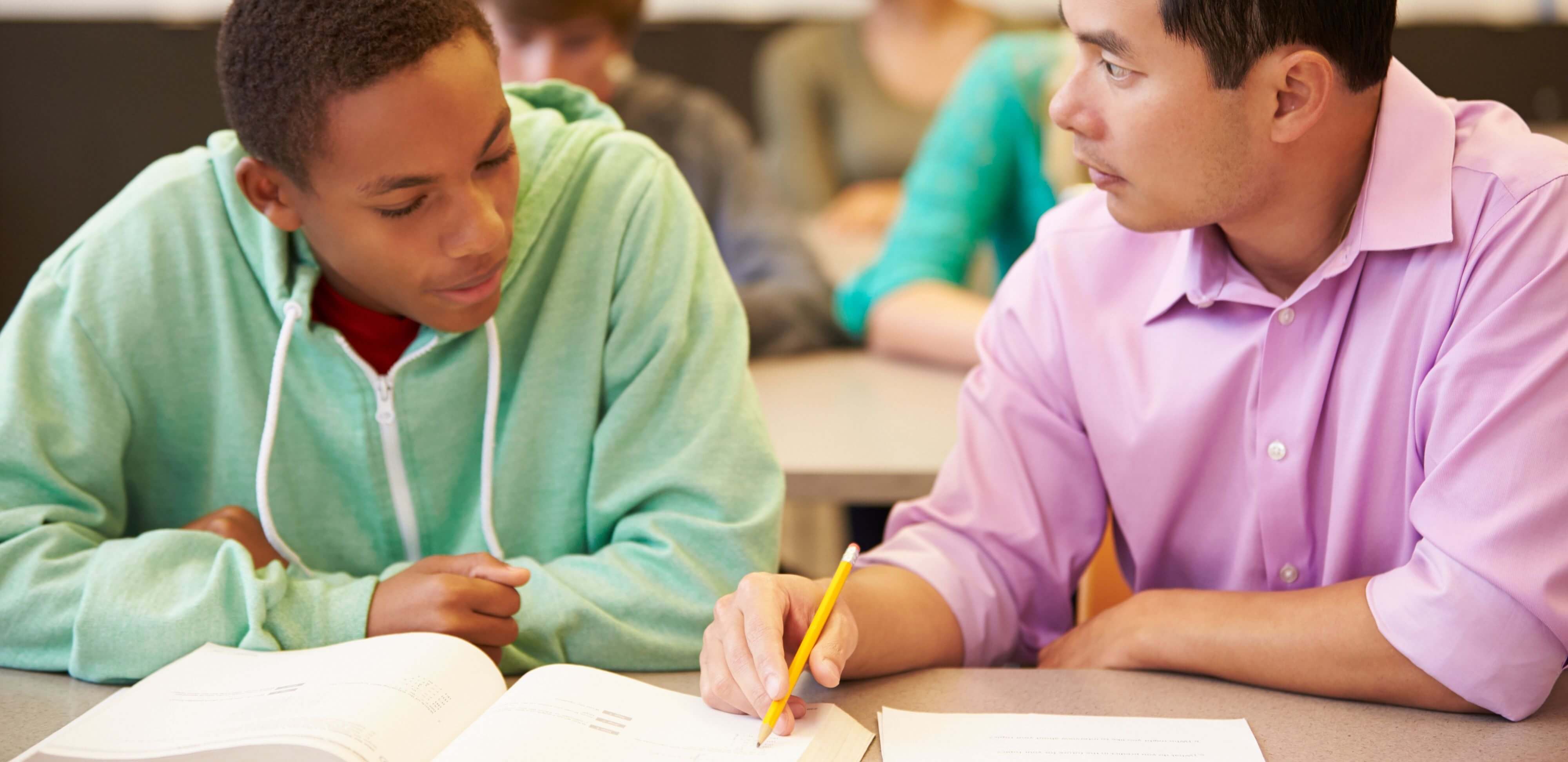 relatório de desempenho escolar: imagem de um professor sentado ao lado de uma aluno adolescente ensinando-o