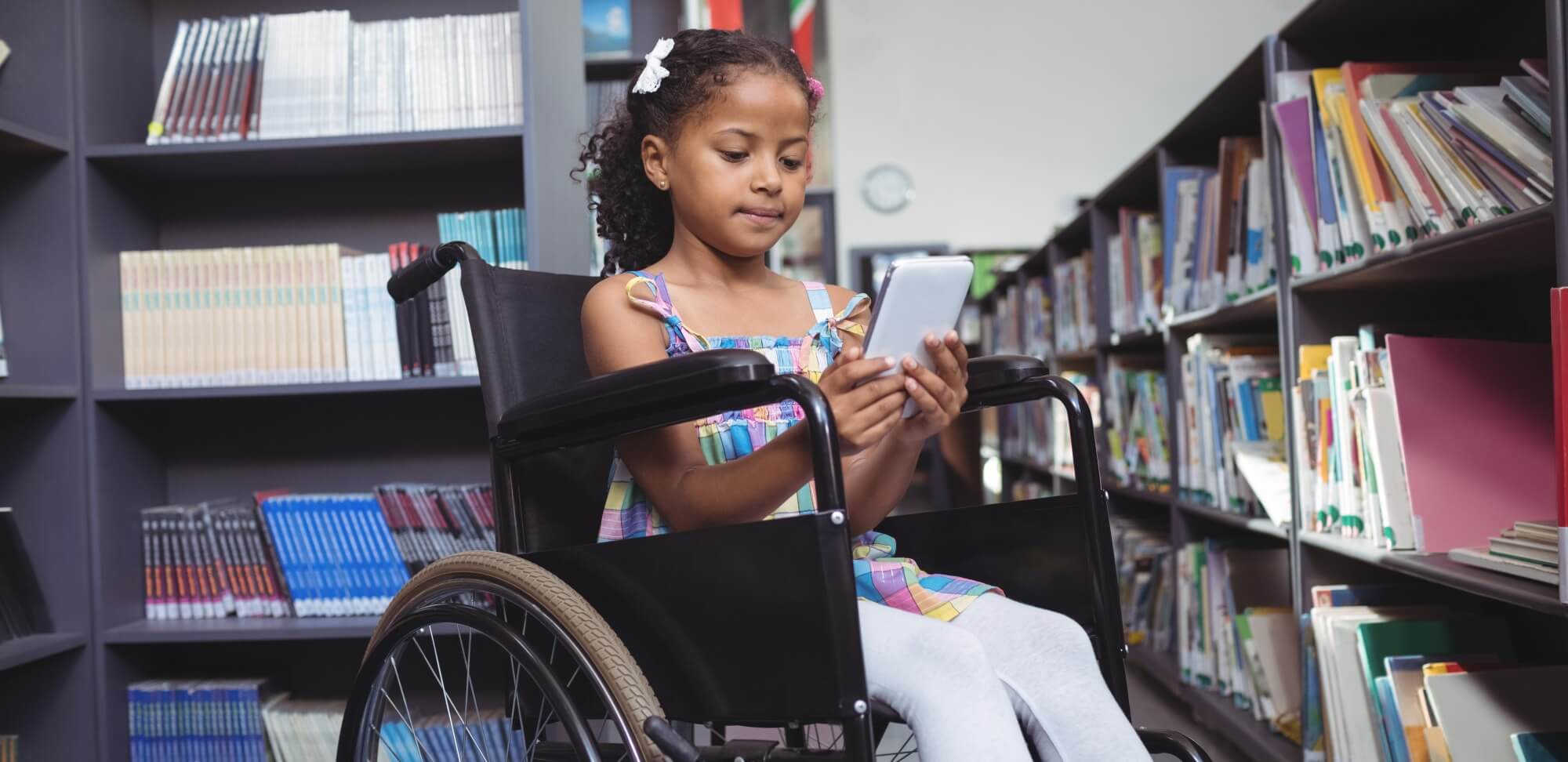 Os desafios da inclusão escolar no cotidiano da escola regular: fotografia de uma menina em uma cadeira de rodas utilizando um tablet em uma biblioteca.