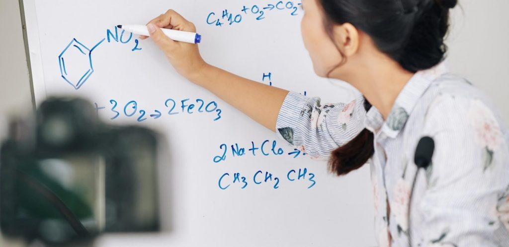 como fazer uma boa videoaula: imagem de uma mulher escrevendo fórmulas químicas no quadro