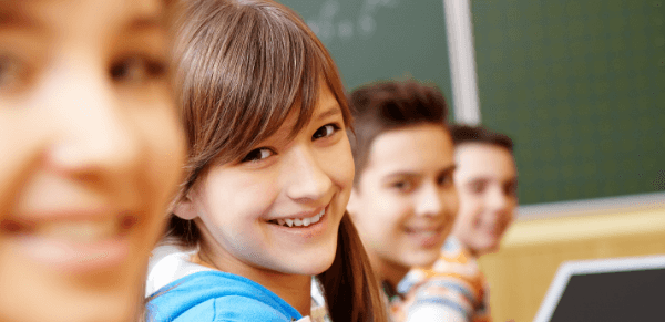 Avaliação da aprendizagem escolar: imagem de quatro crianças sorrindo em sala de aula.