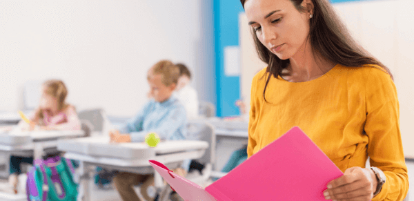 Desafios da BNCC: imagem de uma professora lendo um documento em uma pasta em sala de aula.