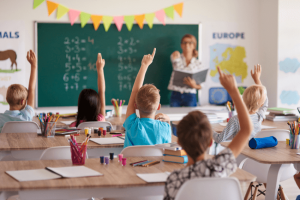 Participação dos alunos em sala de aula: alunos com a mão levantada para responder à professora