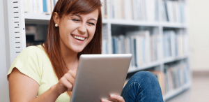 Livros interativos: imagem de uma estudante lendo no tablet sentada em uma biblioteca